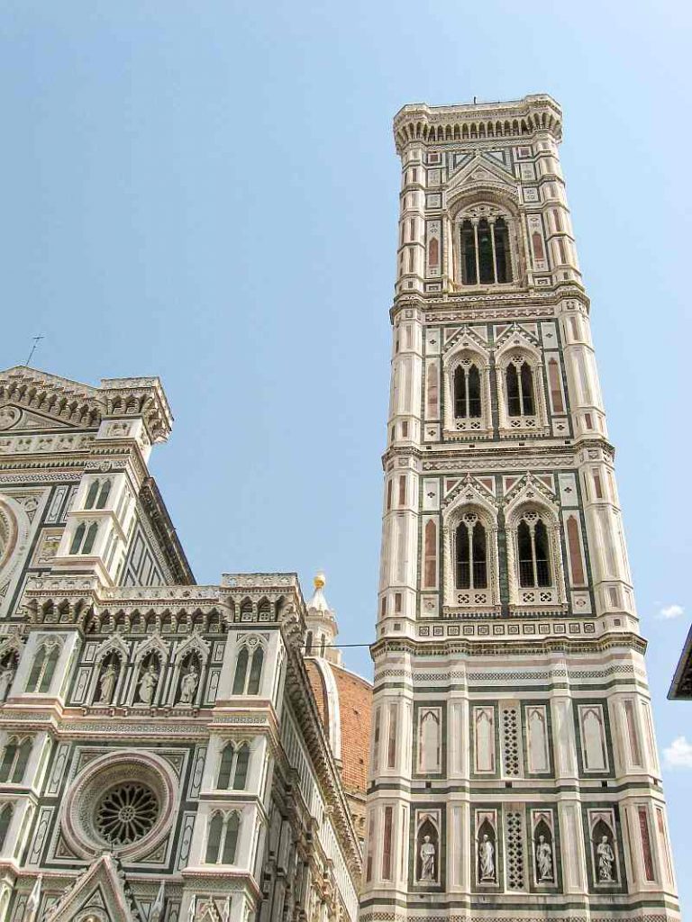 The image shows the Giotto's Campanile, a tall, ornate bell tower with geometric designs, next to Florence Cathedral in Italy, both built in white, green, and pink marble, under a clear blue sky.