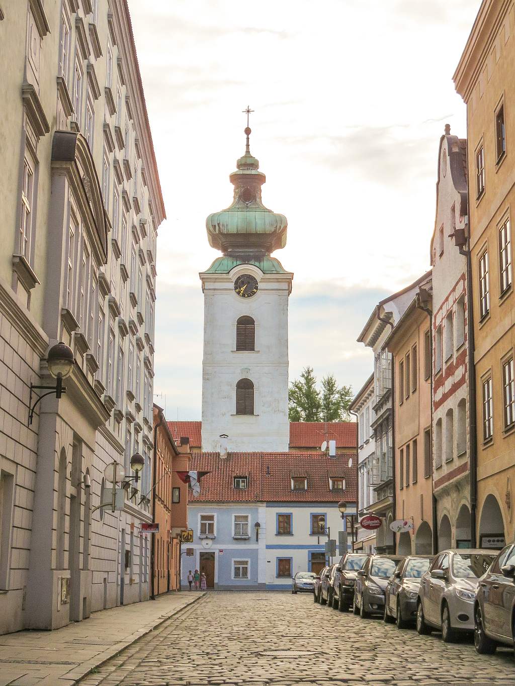 a street with cobbled stones, colourful buildings on both sides and at the end a white tower of a monastery, the tower of the Dominican Monastery in Ceske Budejovice in South Bohemia, Czech Republic