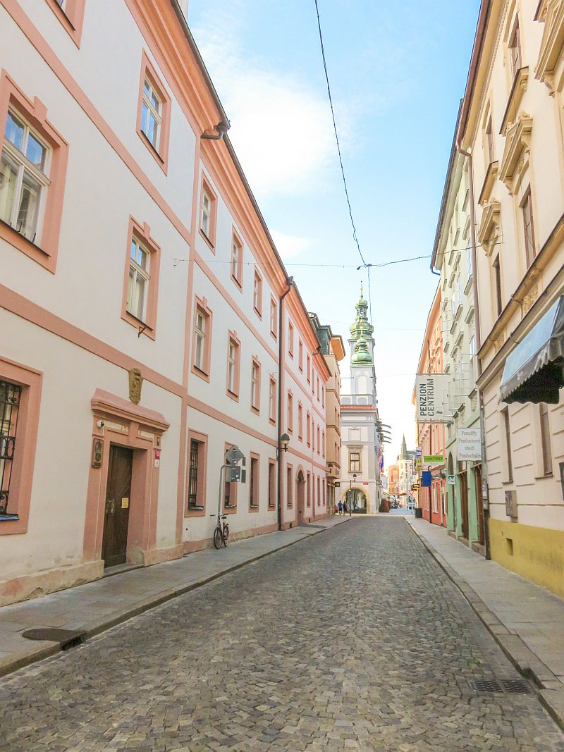 a street leading to a square lined up with buildings with colourful facades in pin, orange, green and peach, a street in Ceske Budejovice in South Bohemia, Czech Republic
