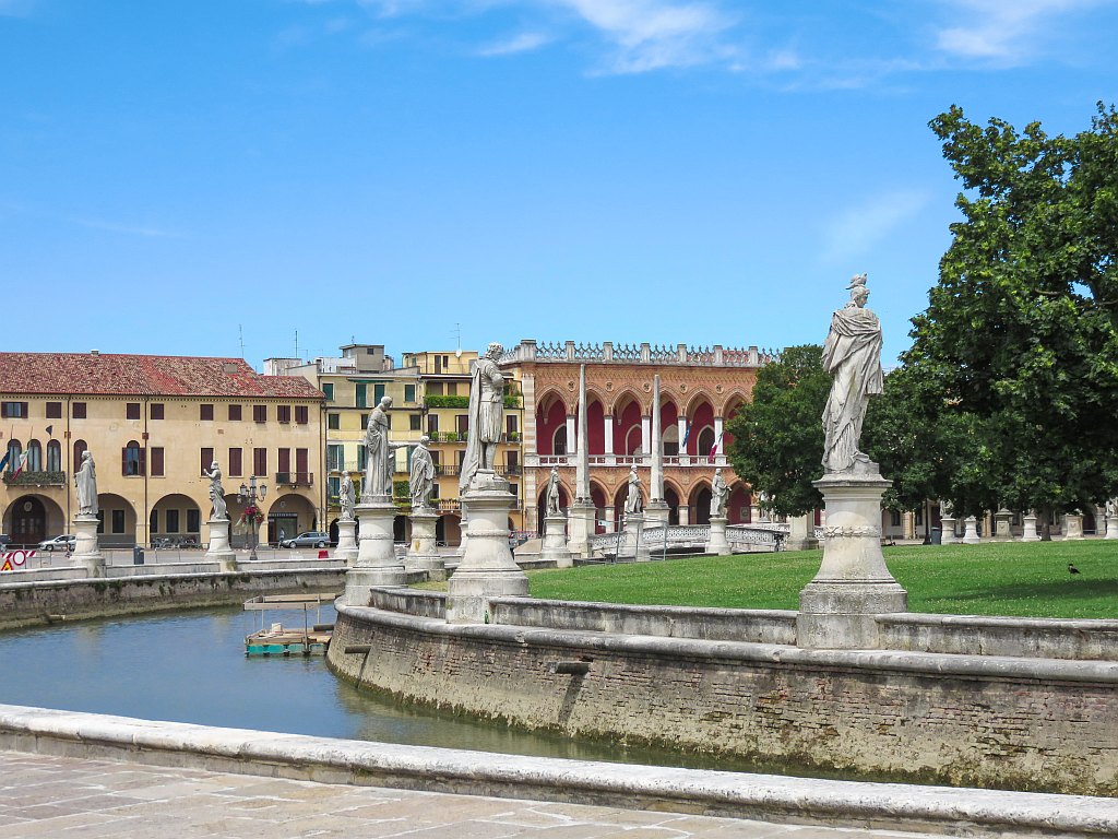 a water feature with statues around it and green in the middle with renaissance buildings at the background, Prato della Valle Square in Padua