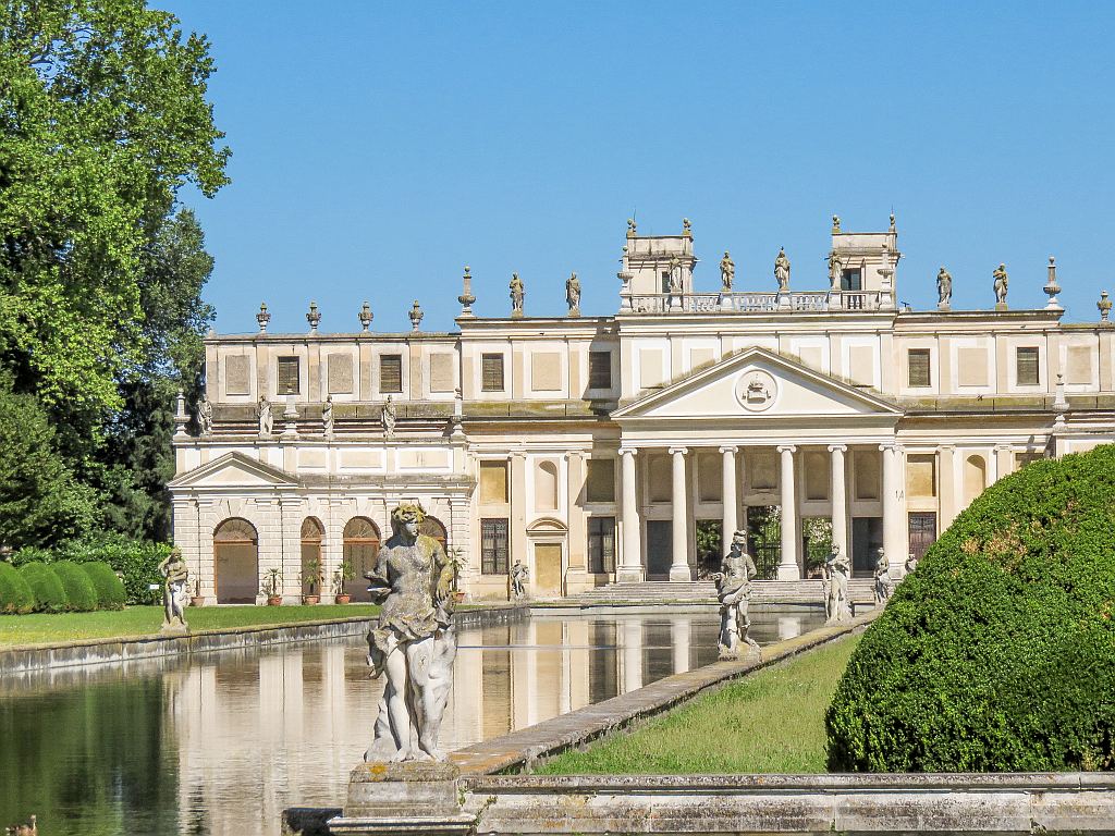 a white large building with columns and water canal in front of it lined up with statues, Villa Pisani along the Brenta Canal
