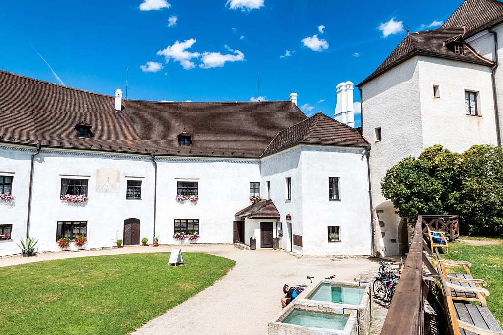 a white chateau as viewed from the yard with green grass in front and pots with flowers on the windows; Nove Hrady Castle