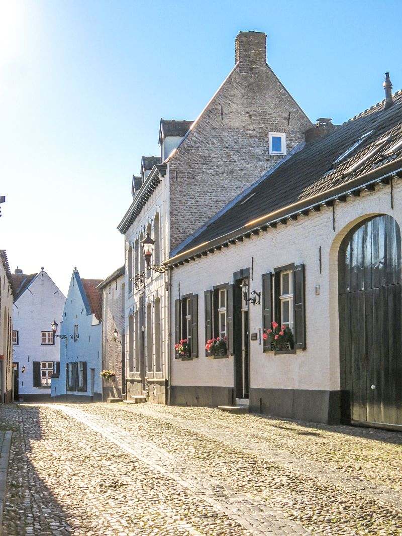 a cobblestone street with whitewashed houses on both sides and geraniums on the windows, early in the morning, Thorn Netherlands