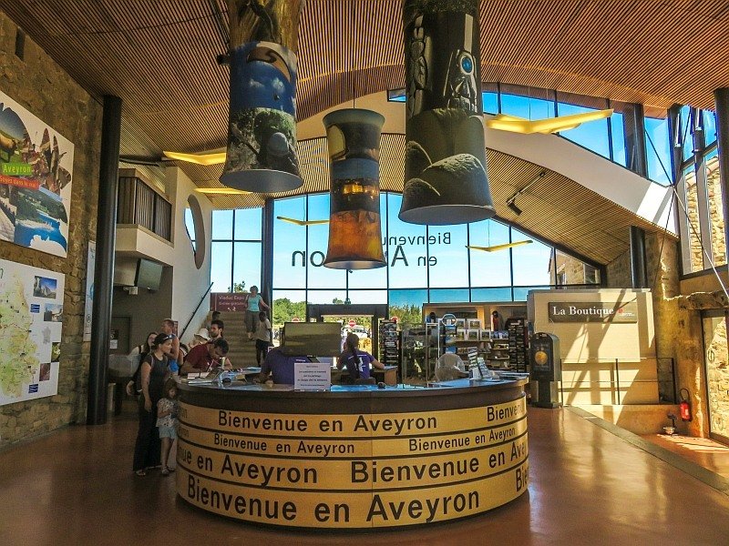 a round counter with a text in French - Welcome in Aveyron, in the foyer of a light building with lots of wooden features, the foyer of the visitors centre at the Millau Viaduct