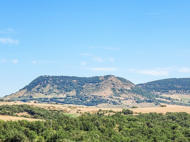 a high plateau with some small green patches of trees and blue sky with hardly any clouds