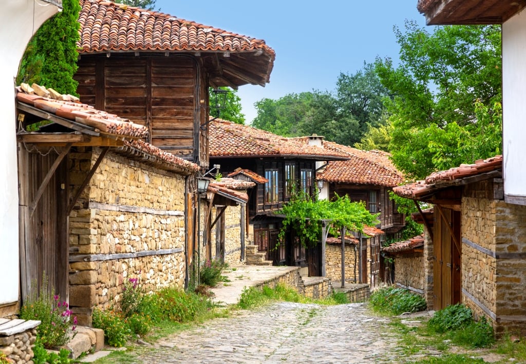 wooden-clad houses with red roof tiles, connected with stone fences, along a cobbled stone street, Zheravna village in Bulgaria