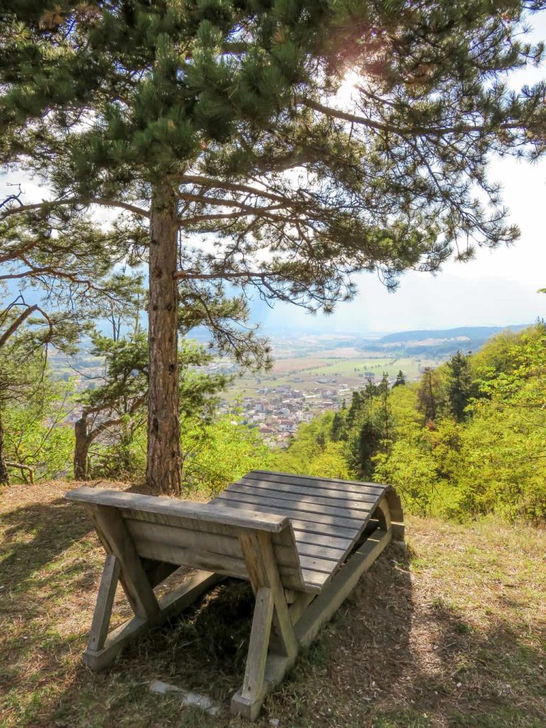 a wooden chaise-longue on a top of a hill with a beautiful view to a valley with mountains