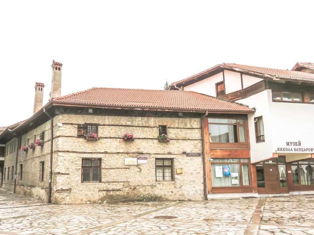 an old stone house with pink geraniums hanging on the windows, the Birthplace Museum of Vaptsarov in Bansko