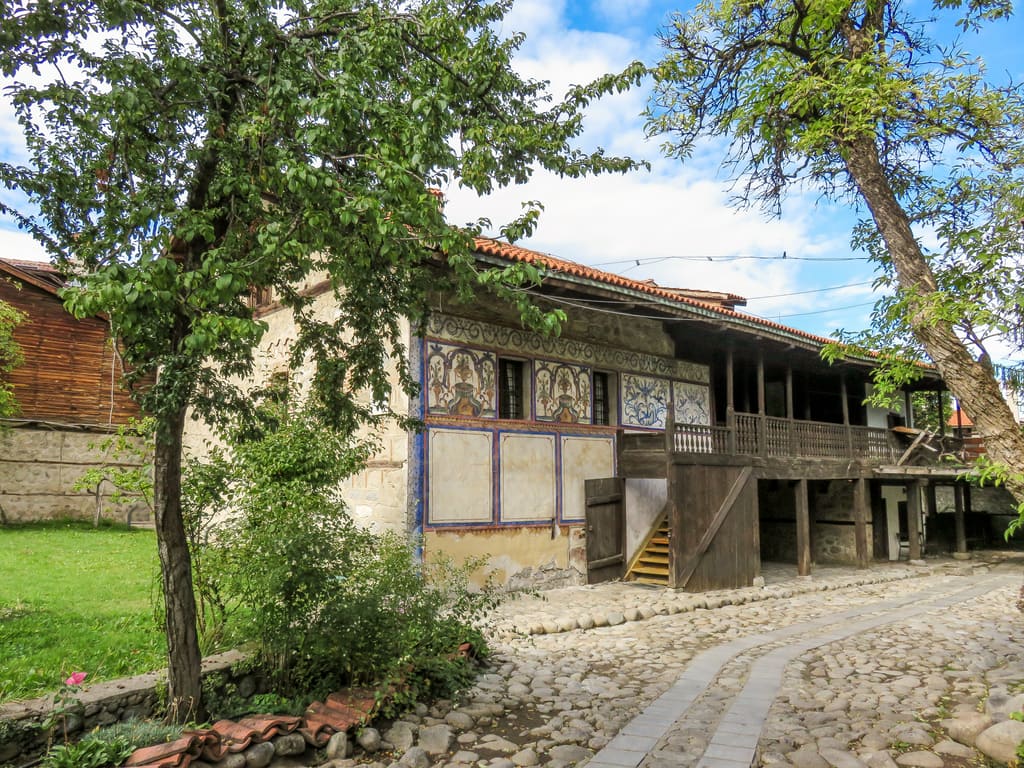 a house in a traditional Bulgarian style with walls painted with decorative motifs and some trees in front, Velyan's house in Bansko