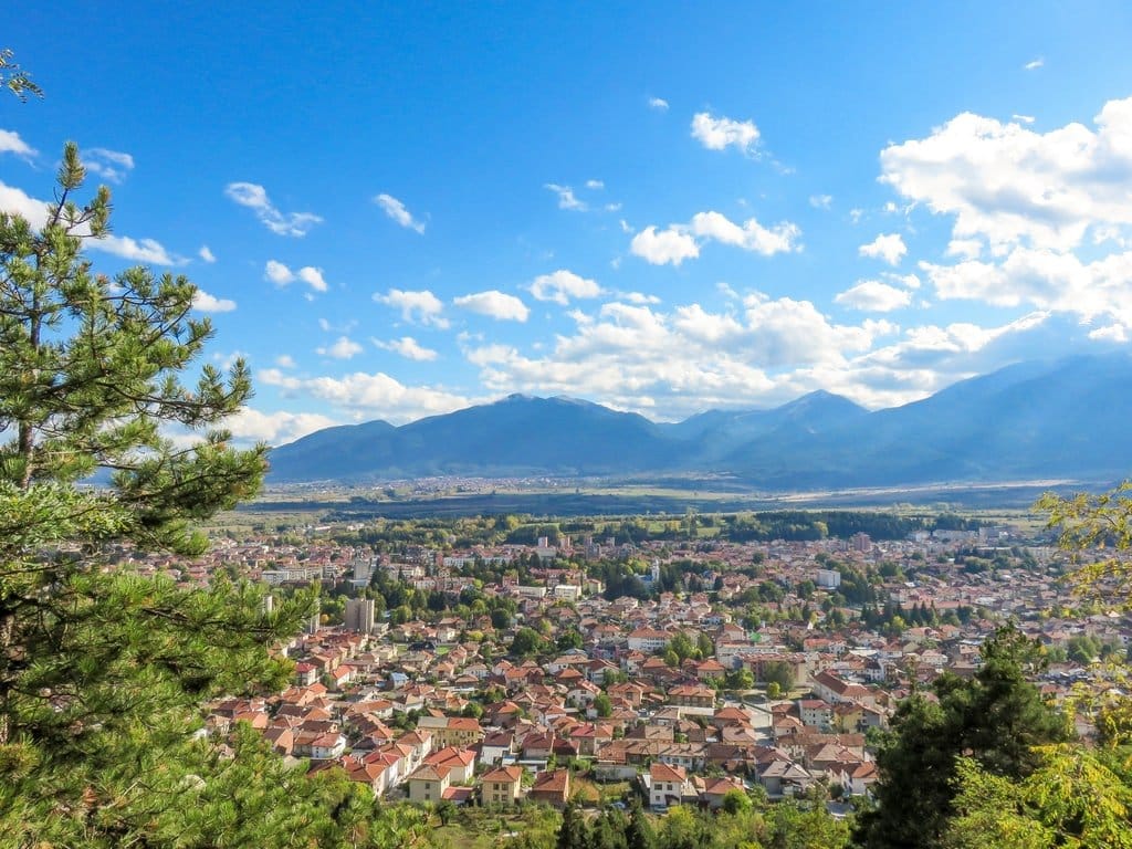 a view from a top of a hill to a town in the valley and a mountain range at the background
