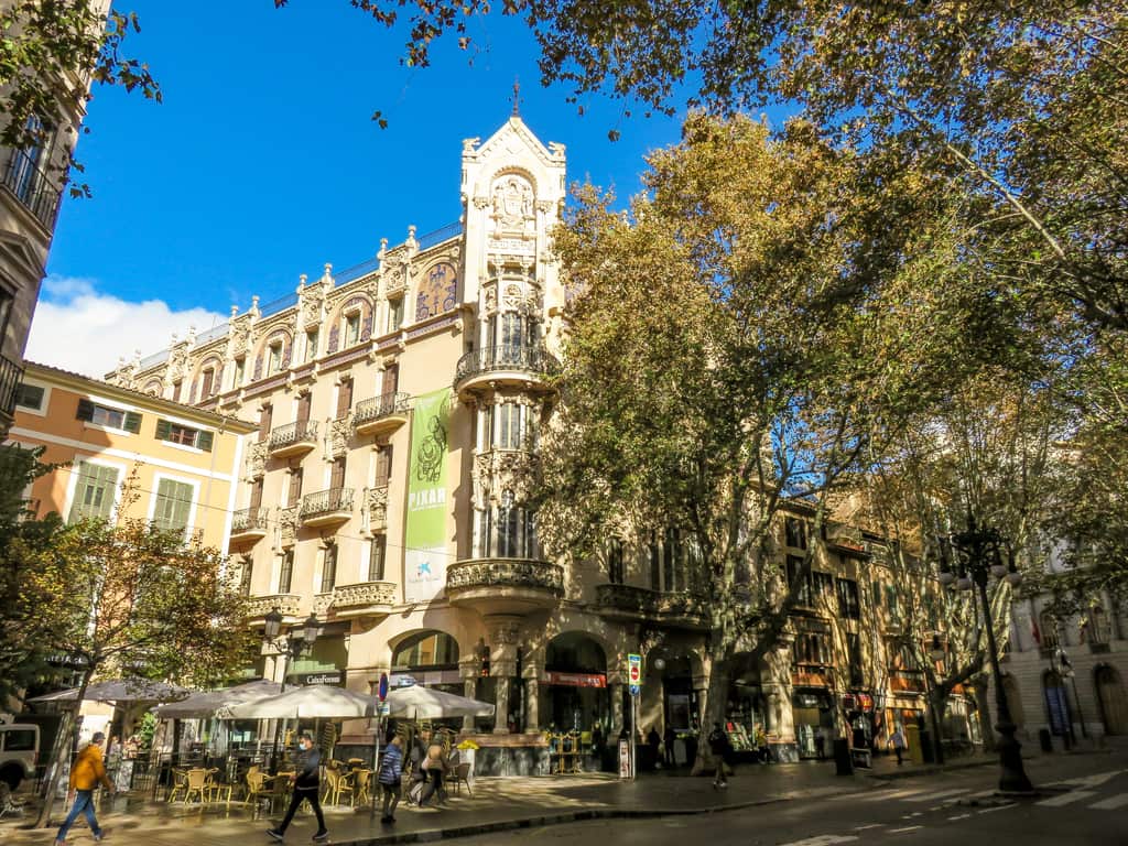 a building in art nouveau style across the street with some trees on both sides of the street, Gran Hotel in Palma de Mallorca, Spain