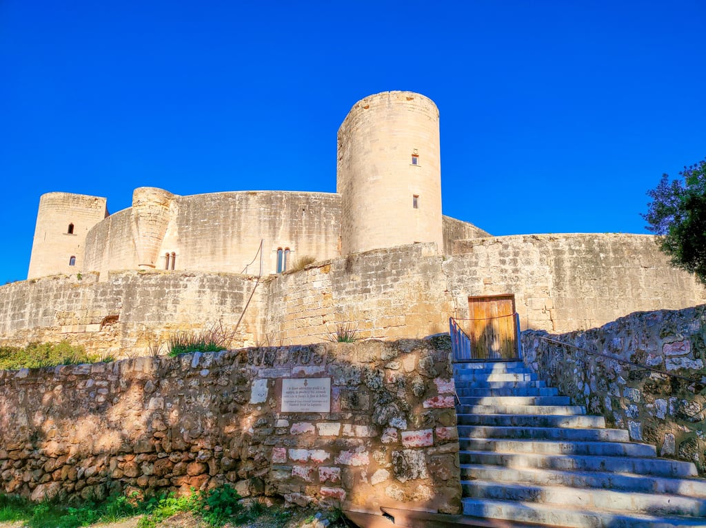 a round castle with round towers and stairs leading to it against a blue sky; Bellver Castle in Palma de Mallorca, Spain