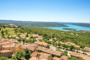 a view from above of a village with a castle on the top of the hill and a lake at the background; view of Aiguines and the Lake of Sainte-Corix
