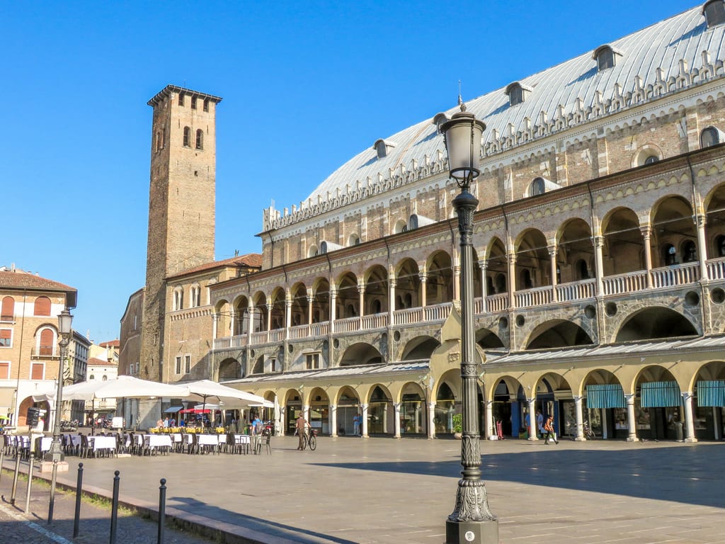 a beautiful porticoed budling with a tower at one end and a square with restaurants tables; Palazzo della Ragione in Pafua