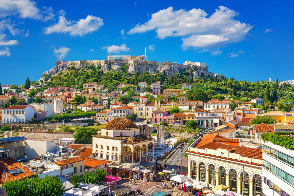 colorful buildings and a green rocky hill with a Greek temple on top; The Monastiraki Square with a view of the Acropolis and the Parthenon - one of the best things to do in Athens, Greece