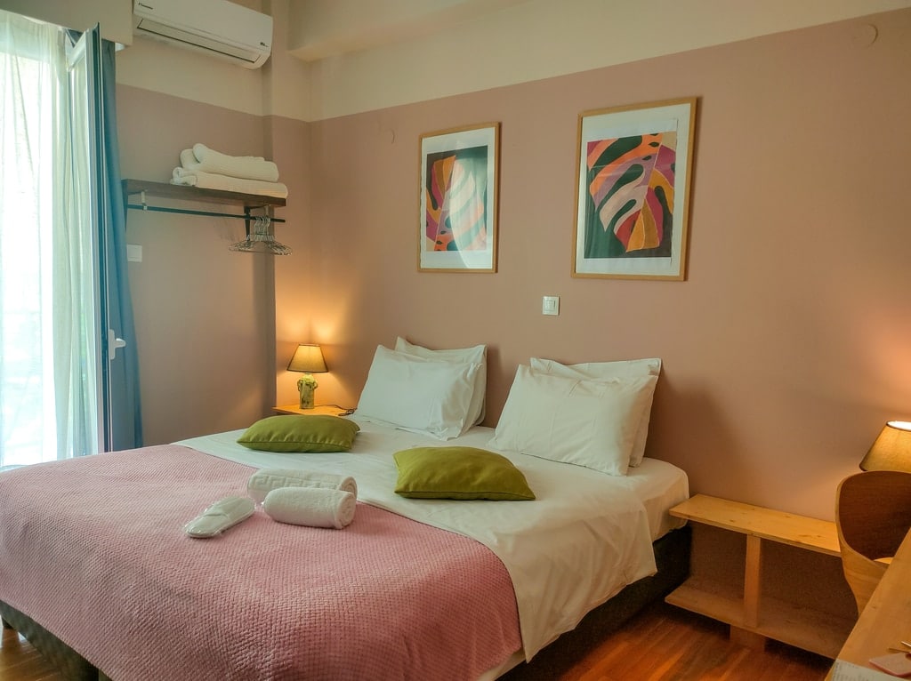 A queen-size bed with pink cover and green cushions in a hotel room. Kalamata Art Hotel