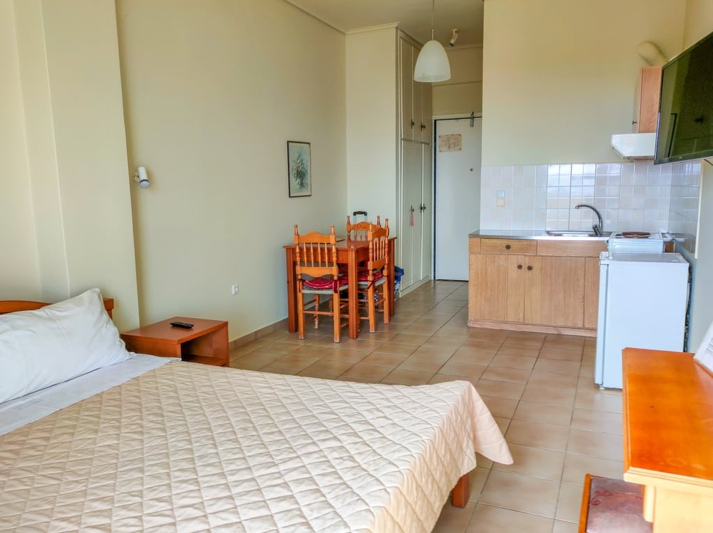 A large studio with a queen-size bed, a table with chairs and a small kitchenette. A room in Hotel Fotini in Kalamta