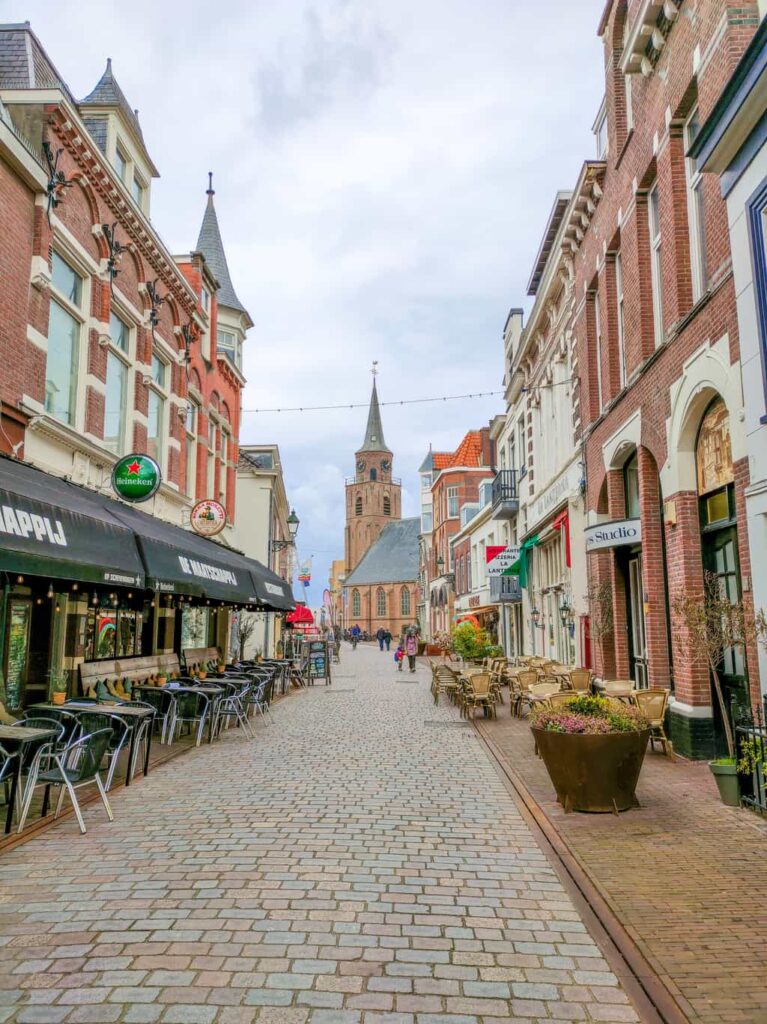 a paved street lined up with shops and restaurants and a church at the end of the street; Keizerstraat in Scheveningen