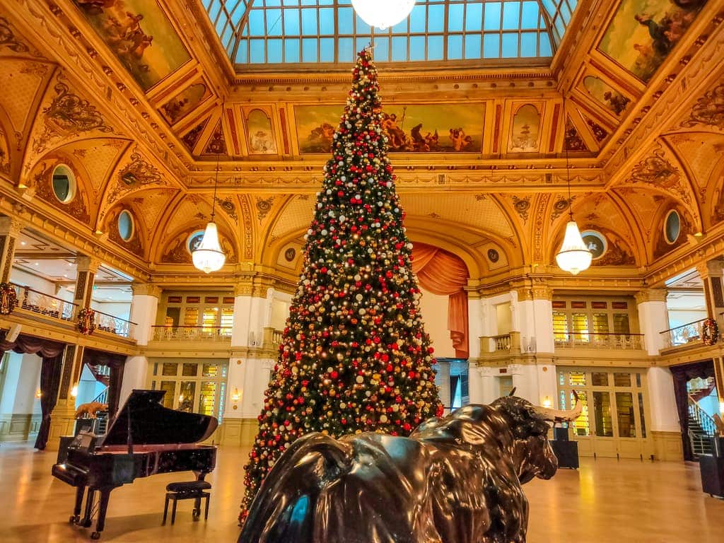a grand hall with a Christmas tree in the middle; a piano and a sculpture of a bull; the interior of the Kurhaus in Scheveningen