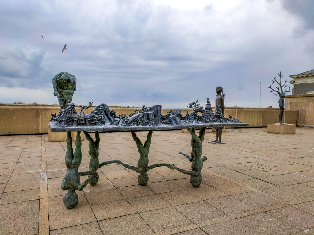 a few different sculptures on a roof of a building with a steel-gray sky above and 2 birds flying; Sculptures at Museum Beelden aan Zee in Scheveningen