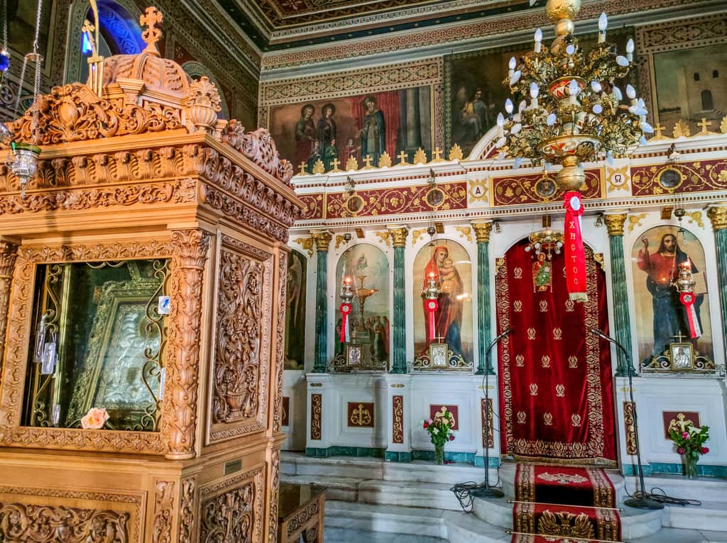 The interior of an ornate Eastern Orthodox church with intricate wooden carvings, religious paintings and icons, and a chandelier. The interior of Panagia Eleistria Church in Koroni.