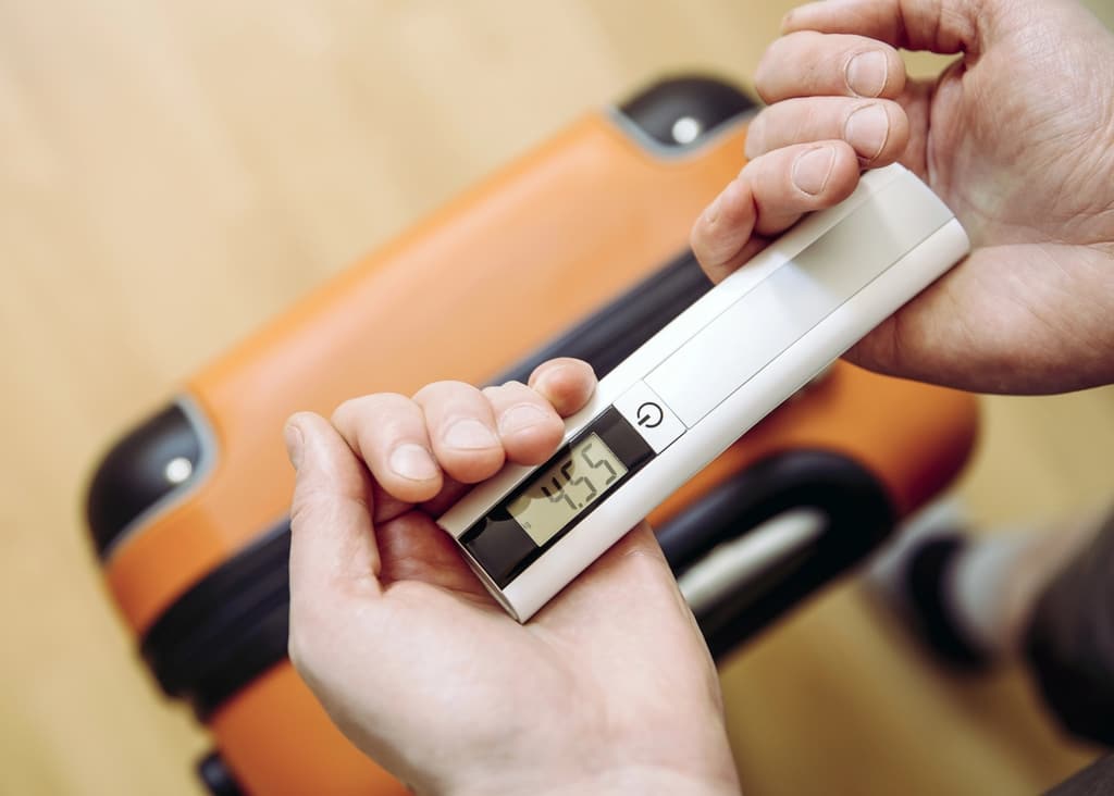 A person holds a digital luggage scale displaying 4.45 while weighing an orange suitcase.